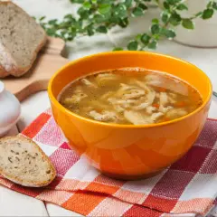 Gorąca zupa flaki w pomarańczowej misce, obok kromki chleba. Idealne do flaków są świeże dodatki.