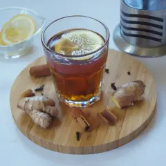 Szklanka herbaty z cytryną, obok świeży imbir, laski cynamonu i goździki. Idealne składniki, by dowiedzieć się, jak dodać imbir do herbaty.