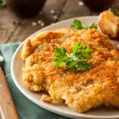 Chrupiący kotlet w złocistej panierce do mięsa, podany z pieczonymi ziemniaczkami i cytryną.