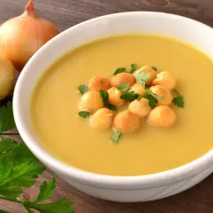 Aksamitna zupa cebulowa, ozdobiona grzankami i natką pietruszki, z cebulami i przyprawami w tle.