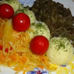 Talerz z wątróbką drobiową, ziemniakami, surówką z kapusty i marchewki oraz pomidorkami koktajlowymi.