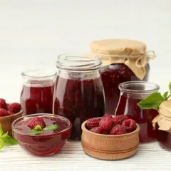 Słoiki z domowym dżemem malinowym i świeże maliny. Idealne na lato, gdy chcesz wiedzieć, jak zrobić sok z malin na surowo.