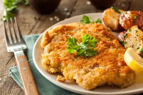 Chrupiący kotlet w złocistej panierce do mięsa, podany z pieczonymi ziemniaczkami i cytryną.