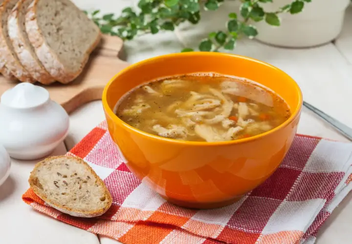 Gorąca zupa flaki w pomarańczowej misce, obok kromki chleba. Idealne do flaków są świeże dodatki.