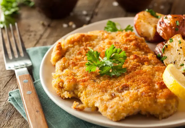 Chrupiący kotlet w złocistej panierce do mięsa, podany z pieczonymi ziemniaczkami i cytryną.